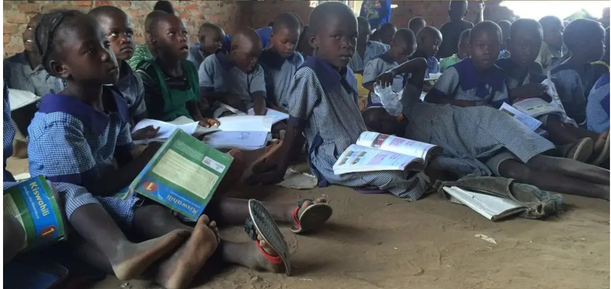 Photo of Learners in a classroom sitting on the floor holding study materials on their laps